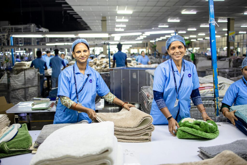 Regulations and Certifications Shaping Ethical Manufacturing, Two female workers in a textile factory sorting and organizing towels on a production line.